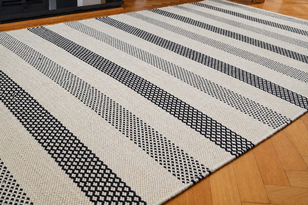 Angled view of the black and ivory flatwoven wool kilim rug, showing its diamond-stripe pattern — retouched photo