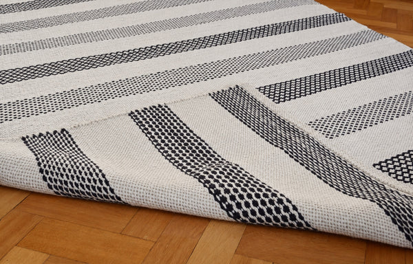 Folded corner of the black and ivory wool kilim rug showing the reversible weave and hemmed edge — retouched detail